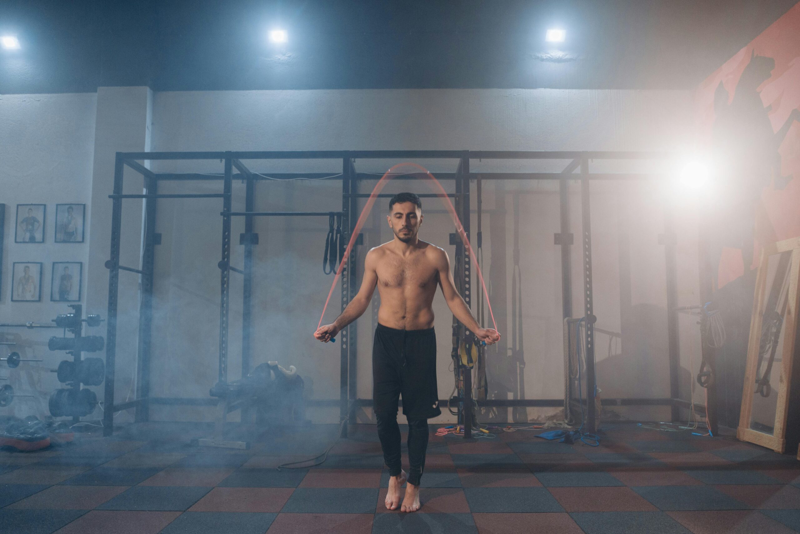 A shirtless male athlete jumping rope in a gym with a foggy ambiance.